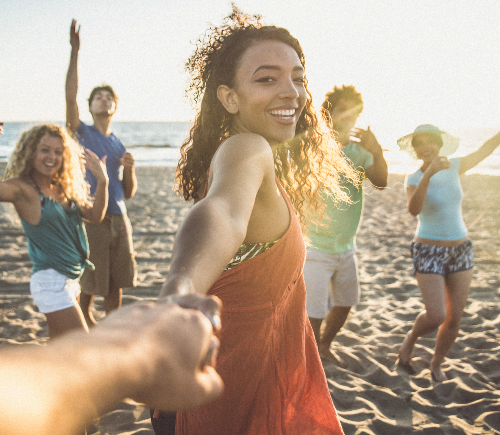 Une femme tient le bras d'une personne. Elle est sur la plage et entourée d'amis.